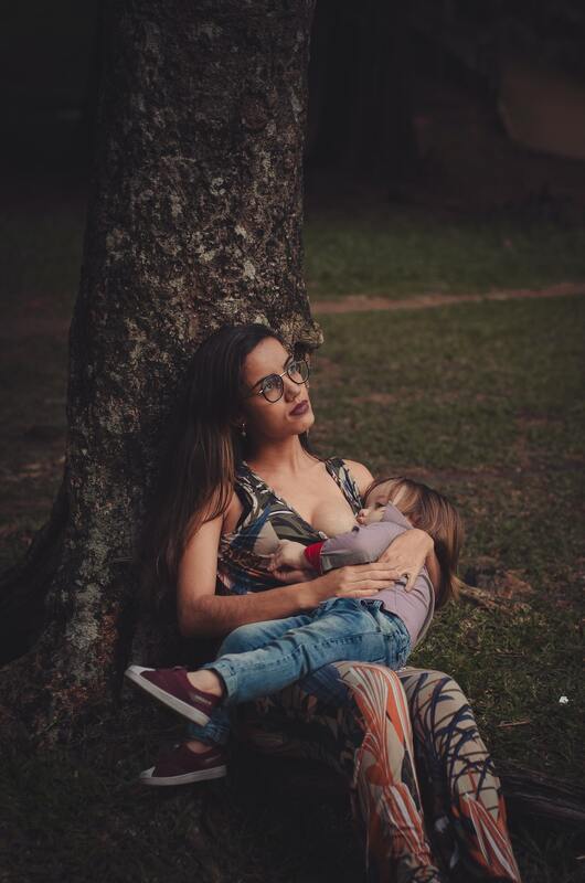 woman leaning against tree and nursing a toddler